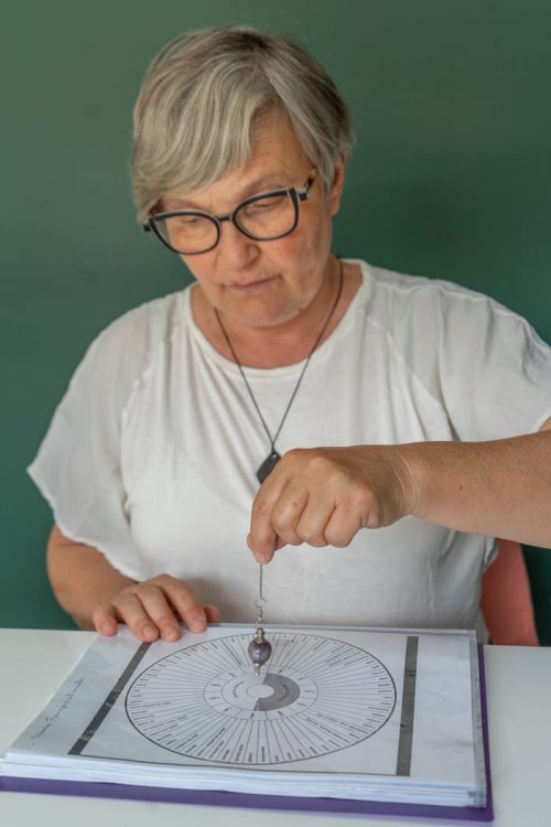 Pascale travaillant avec son pendule sur des fiches de géobiologie